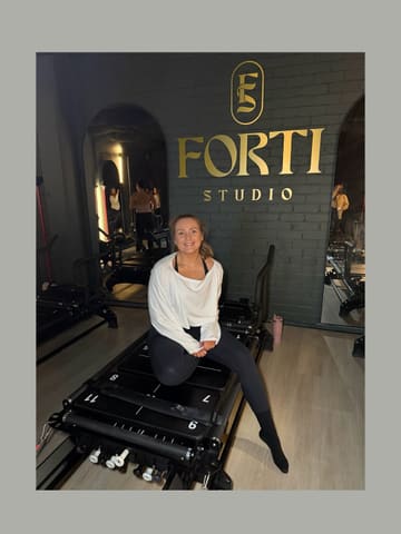 A photo of a creator sitting on a reformer pilates machine at Forti Studio, posing for the camera.