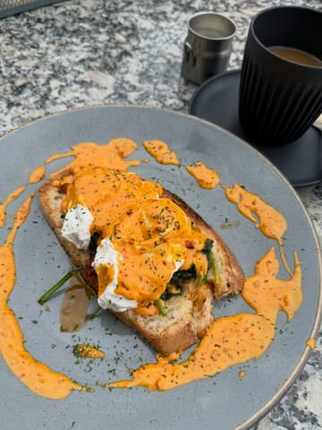 An overhead, natural-light shot of an Nduja Eggs Benedict dish served with a coffee, captured on an outdoor table.