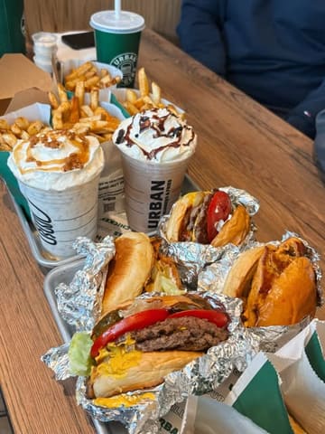 A high-angle, overhead shot of a table spread featuring a variety of fast food items including burgers, fries, sides, and milkshakes from Urban Burger. The image captures a 'feast' style presentation, typical of a casual dining review.