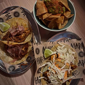 A top-down, casual shot of Mexican food including tacos and guacamole with chips, served on branded paper.