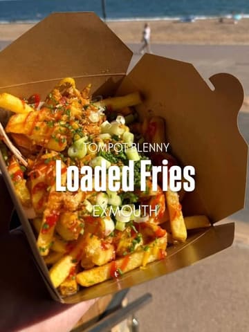 A simple, effective shot of loaded fries held in front of a beach backdrop, clearly communicating the casual, seaside nature of the venue. The lighting is natural and bright, highlighting the textures of the food, while the background provides context without distracting from the main subject.