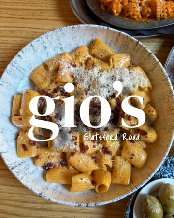 A high-angle, top-down food photography shot of a bowl of rigatoni pasta with a rich, reddish sauce, topped with grated cheese and herbs. A small bowl of olives is visible in the bottom right corner, and another pasta dish is partially visible at the top. The image features a prominent white text overlay branding the venue as 'gio's' with the location 'Slateford Road'.