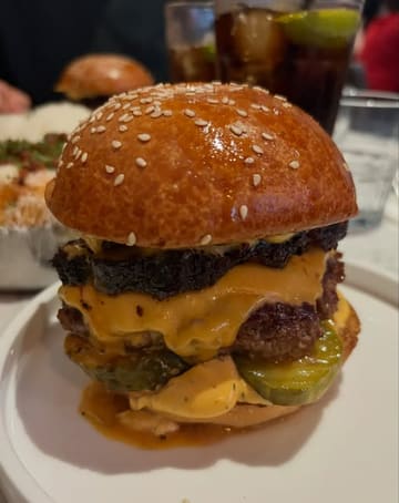 A close-up, eye-level shot of a stacked burger in a restaurant setting, focusing on the texture of the bun and the layers of the patty and cheese.