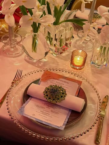 A sophisticated, atmospheric shot of a table setting at The Ivy Asia, showcasing the 'Elements Menu'. The image features elegant floral arrangements, a candle, and a neatly placed menu, capturing a high-end, moody dining environment.