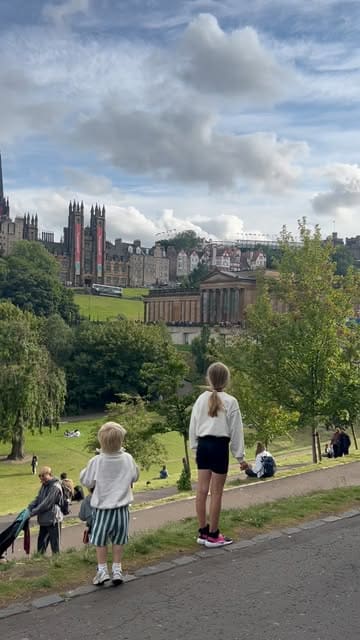 A candid, outdoor lifestyle shot taken in Edinburgh, likely Princes Street Gardens, capturing children looking out towards the city skyline during the Edinburgh Fringe festival. The image serves as a travel and family-oriented snapshot, documenting a day trip.