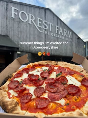 A casual, first-person perspective shot of a pepperoni pizza in a takeaway box, held up in front of the Forest Farm building. The image serves as an introduction to a list of summer recommendations in the Aberdeen area.