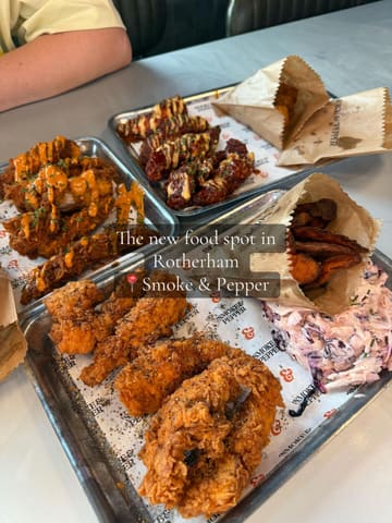 A top-down, slightly angled shot of multiple trays of fried chicken, wings, and sides from Smoke & Pepper in Rotherham, presented on branded paper.