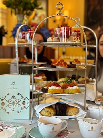 A high-quality, elegant shot of an afternoon tea service at The Shelbourne, featuring a tiered stand with sandwiches, scones, and desserts.