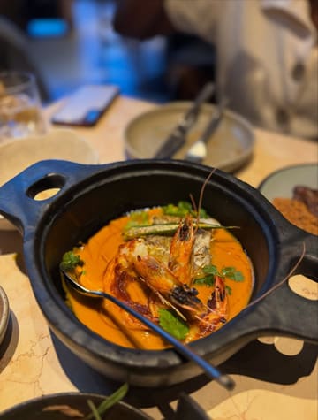 A close-up, high-quality shot of a seafood moqueca served in a dark, rustic bowl, highlighting the vibrant orange sauce and fresh prawns.