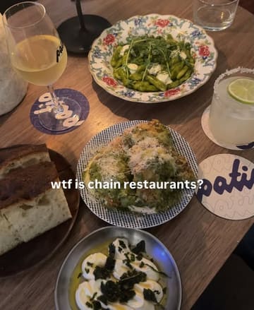 A flat-lay shot of a dinner spread featuring pasta, bread, a dip, and drinks, likely at an independent restaurant in Brighton. The image captures a casual dining experience with a focus on supporting local businesses over chains.