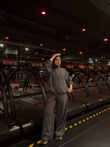 A portrait of a person standing in a Barry's fitness studio, surrounded by rows of treadmills under the brand's signature red lighting. The subject is wearing activewear, highlighting the fitness-focused setting.
