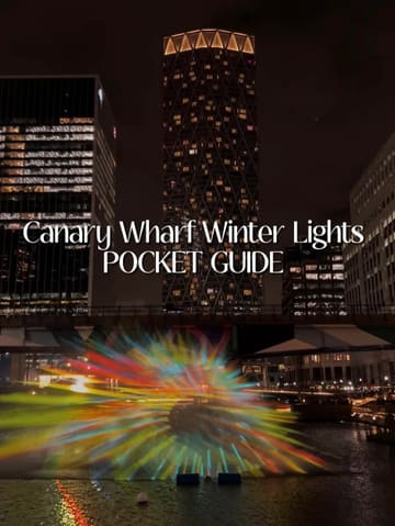 A visually striking night-time shot of a light installation at Canary Wharf, serving as a cover image for a guide to the Winter Lights event. The composition effectively frames the colourful projection against the dark, illuminated city skyline.