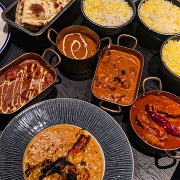 A flat-lay photograph of an Indian restaurant spread featuring various curries, rice, and naan bread.