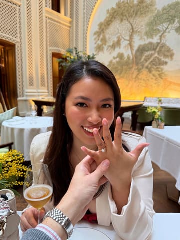 A high-quality, well-composed lifestyle shot capturing an engagement celebration at a luxury hotel. The focus is sharp on the ring, with the subject's expression conveying joy, set against an elegant, well-lit background.