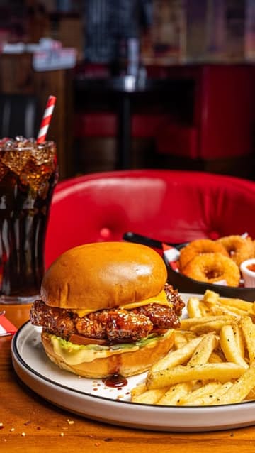 A high-quality, professional food photography shot showcasing a burger, fries, onion rings, and a drink, typical of a casual dining restaurant setting.