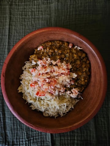 A top-down shot of a homemade bowl of dhal served with rice and a coconut sambal topping, presented in a rustic bowl on a dark textured cloth.