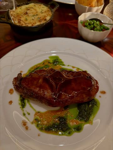 A high-quality, moody shot of a lamb chop main course served with a side of potato dauphinoise and peas, captured in a fine-dining restaurant setting.