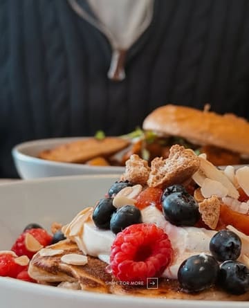 A close-up, appetizing shot of fruit-topped pancakes at Parx Café, with a blurred background featuring a person in a black sweater.