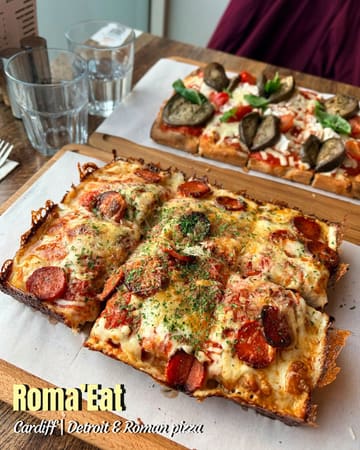 A high-quality, well-lit overhead shot of two different styles of pizza (Detroit and Roman) served on wooden boards at a restaurant, showcasing the textures of the crusts and toppings.