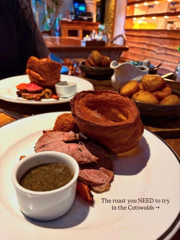 A close-up, slightly overhead shot of a Sunday roast featuring lamb, a large Yorkshire pudding, and roast potatoes, with a second plate visible in the background.