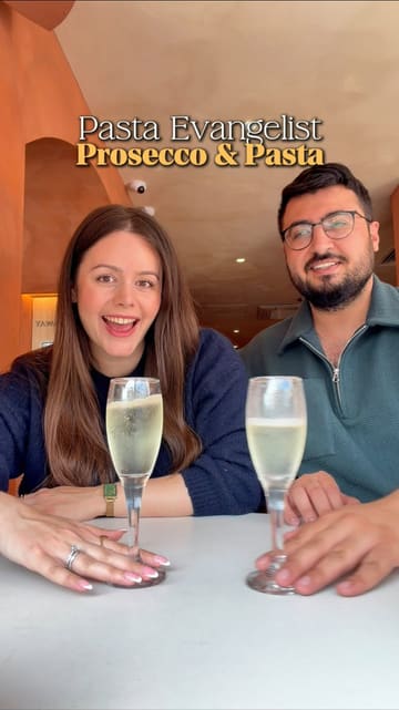 A couple reviews their dining experience at Pasta Evangelists, highlighting the 'build your own pasta' concept. They showcase various dishes including garlic and chilli king prawns, aubergine parmigiana, chicken and mushroom tagliatelle, truffle cacio e pepe, and desserts like tiramisu and strawberry cheesecake, all paired with prosecco.