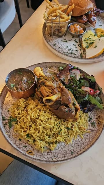 The video is a short, music-driven montage featuring a visit to Monaco Cafe. It highlights the interior, a variety of drinks, and specific dishes including lamb kabsa, a chicken burger with fries, and a baklava dessert. The creator is featured throughout, providing a personal touch to the venue tour.