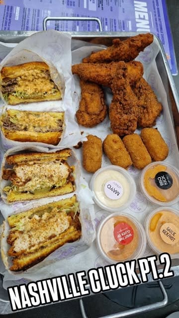 A food review video featuring two men in a car trying various menu items from The Nashville Cluck, including cheese bites, chicken tenders, and burgers.
