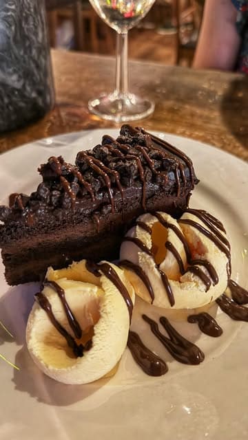 A montage video showcasing a visit to Table 23 in Upminster, featuring shots of a large sharing platter, wine, the restaurant interior, live entertainment, and dessert.