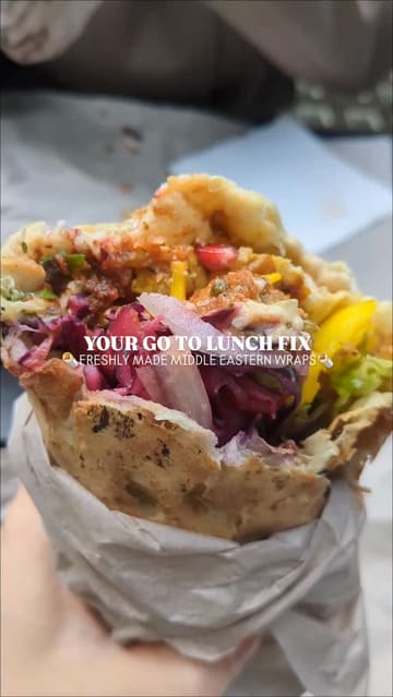 A short, handheld-style video showcasing the preparation and consumption of a Middle Eastern wrap at Zawa. The video highlights the fresh bread-making process, the variety of salad and sauce options, and the final product, ending with the creator enjoying the meal.
