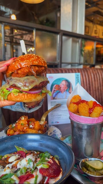 A promotional video for a collaboration menu between Poppy Cooks and Bill's restaurant. The video features close-up shots of a burger, loaded tater tots, a potato salad, and two cocktails, set to music with text overlays highlighting the items.
