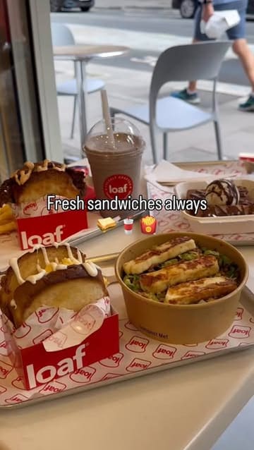 A short, energetic review of a sandwich shop called Loaf, featuring close-ups of their smash burger, truffle scrambled egg sandwich, halloumi salad, and French toast sticks.