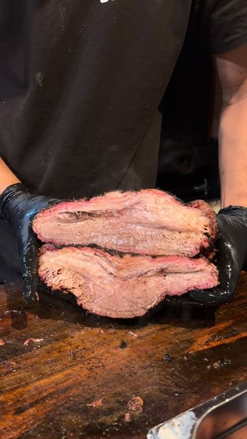 A close-up video of a person slicing a large, tender piece of smoked brisket, demonstrating its texture and juiciness. The video focuses entirely on the food preparation.