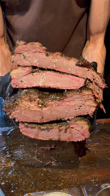 A close-up, handheld video featuring a staff member slicing a large, juicy piece of smoked brisket. The video uses a voiceover to engage the audience by asking about their favorite foods, focusing entirely on the preparation and quality of the meat.