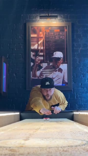A high-energy review of Newhall Street Tavern in Birmingham, featuring the creator sampling various dishes like pizza, meatballs, and fried chicken, while highlighting the venue's shuffleboard games and drink selection.