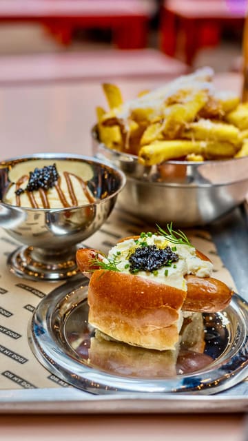 The creator reviews a new 'bougie' caviar-topped hotdog and sundae special from Oh My Dog, available at Seven Dials Market and Lord Napier Star. The video features close-ups of the food preparation, the creator's reaction, and a unique 'hack' involving dipping truffle fries into the sundae.
