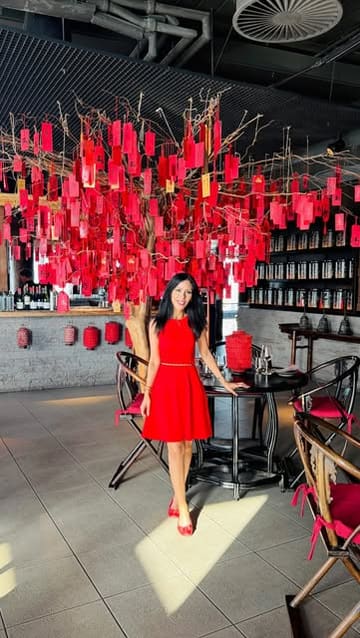A professionally captured, high-quality photograph of a woman posing in a sophisticated, red-themed restaurant interior. The composition is balanced and clean, effectively showcasing the venue's elegant decor and upscale atmosphere.