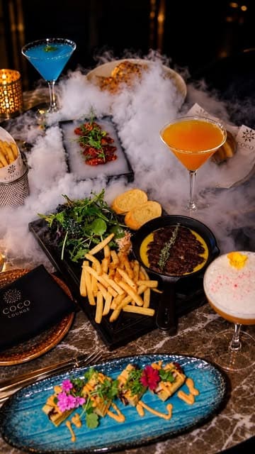 A high-quality promotional montage for Coco Grill & Lounge, featuring a variety of dishes including a signature butter steak, pasta, and desserts, alongside cocktails, set against an upscale, atmospheric backdrop.