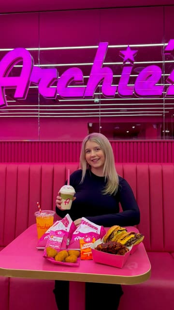 A promotional video featuring a creator at Archie's restaurant, showcasing their smash burgers, shaker fries, chicken strips, and milkshakes. The video uses a mix of close-up food shots and shots of the creator to highlight the menu items and the brand's vibrant pink aesthetic.