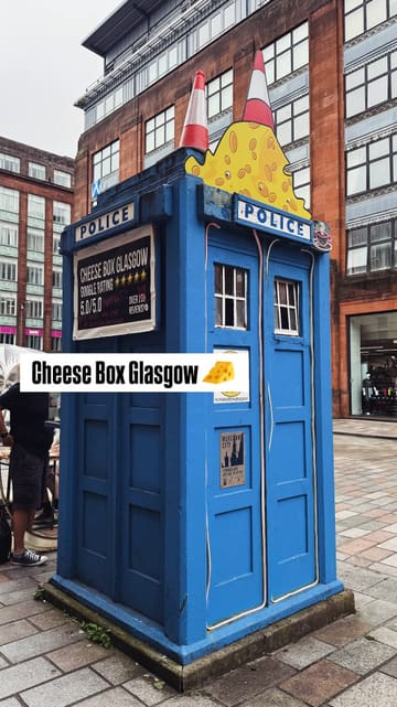 A short, punchy reel featuring a street food stall operating out of a converted police box in Glasgow. The video focuses on the preparation of raclette cheese toasties, showing the cheese being melted and scraped, and includes shots of the unique outdoor seating in a clear dome tent.