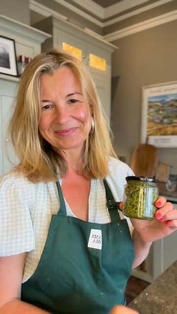A home cooking tutorial demonstrating how to make fresh pesto using a food processor, featuring basil, cashews, parmesan, garlic, and olive oil.