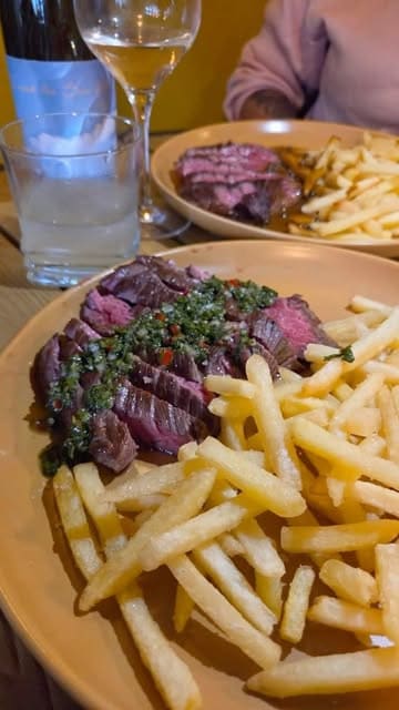 A short promotional video showcasing a steak and frites event, featuring clips of sauce preparation, steaks searing on a grill, and the final plated dishes.