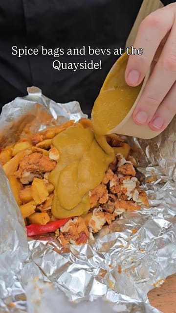 A casual, handheld-style video showcasing a visit to a riverside venue featuring 'spice bags' from a food vendor and drinks. The video includes shots of the food being prepared with curry sauce, the menu, the drinks, and the scenic quayside location.