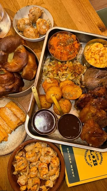 A vlog-style video featuring two creators visiting Las Bombas to try their Latin American-inspired Sunday roast platter, showcasing the venue's interior, menu, and food.