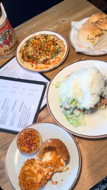 A review of the new menu at Ornella's Kitchen in Manchester, featuring a variety of dishes including hummus, focaccia, arancini, crispy chicken caesar salad, crab linguine, and beef short rib with gnocchi.