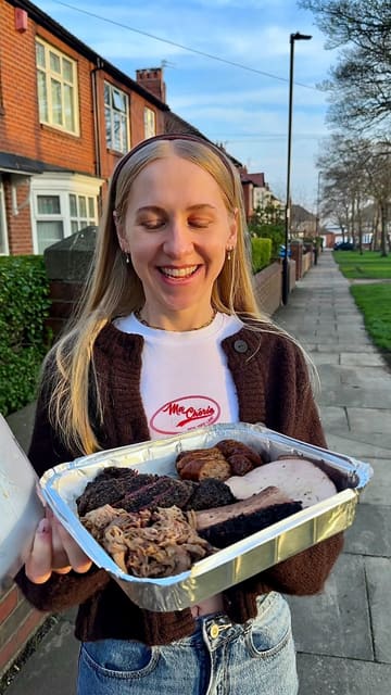 A creator reviews a large BBQ sharing tray from Big Norms, highlighting the variety of smoked meats including brisket, beef cheeks, turkey, and sausage, alongside sides like mac and cheese. The video features close-up shots of the food, the traditional smoker, and the creator enjoying the meal.