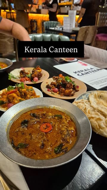 A short, engaging video featuring a creator visiting Kerala Canteen in Leeds. The video highlights the restaurant's atmosphere, interior, and a selection of their new menu items, including beef curry, paneer pepper fry, and chili and tamarind cauliflower.