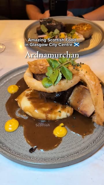 A review of Ardnamurchan in Glasgow, highlighting their focus on sustainable Scottish produce. The video features close-ups of various dishes including scallops with pork belly, a pear and blue cheese salad, venison, beef short rib, and a Scottish cheese board, alongside shots of the restaurant interior and the creator's commentary.