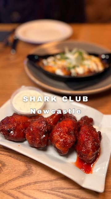 The video is a short, voiceover-led review of Shark Club in Newcastle, highlighting a specific set menu deal. It features quick cuts of various dishes including wings, a burger, buffalo chicken pizza, and desserts, alongside shots of the bar area and sports screens.