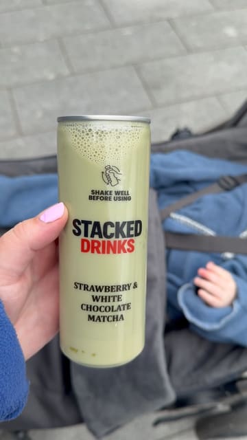 A short, handheld vlog-style video showing a visit to 'The Alcohol Company' off-license to purchase 'Stacked Drinks' matcha cans. The creator walks into the store, highlights the fridge display, and shows the product.