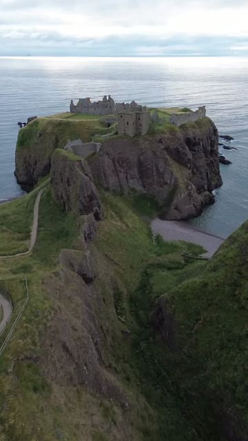 A single, continuous drone shot capturing the exterior of Dunnottar Castle, a medieval fortress situated on cliffs overlooking the North Sea in Scotland.